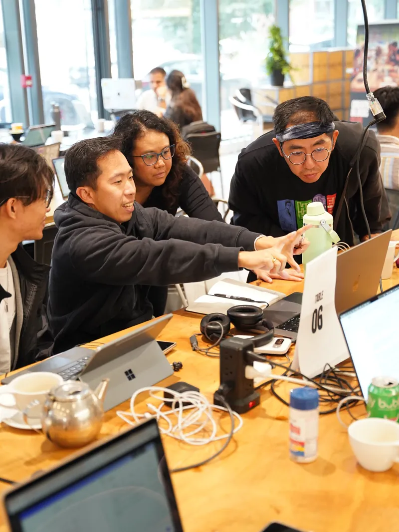 Four members leaning in around a laptop during a session.